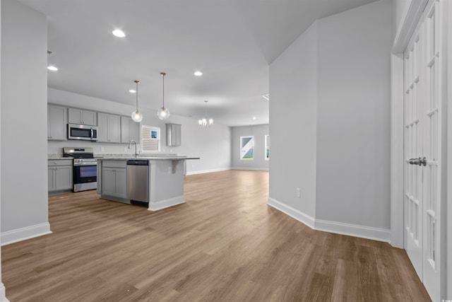 kitchen with a chandelier, wood finished floors, stainless steel appliances, open floor plan, and gray cabinetry