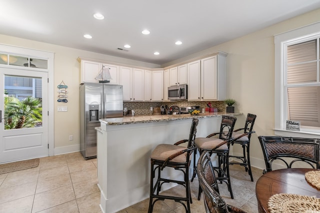kitchen featuring recessed lighting, a peninsula, backsplash, light stone countertops, and appliances with stainless steel finishes