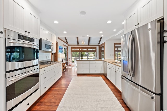 kitchen featuring dark wood finished floors, a peninsula, white cabinetry, a sink, and stainless steel appliances