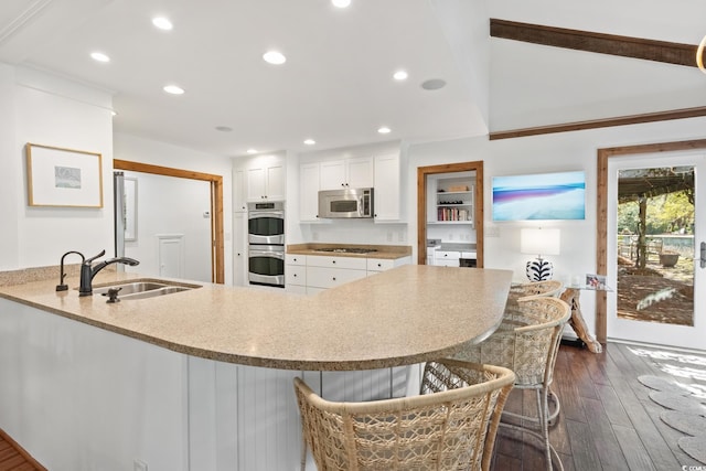 kitchen featuring white cabinetry, appliances with stainless steel finishes, a sink, a breakfast bar area, and dark wood-style floors
