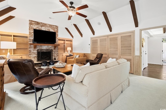 carpeted living area featuring visible vents, ceiling fan, wooden walls, wainscoting, and vaulted ceiling with beams
