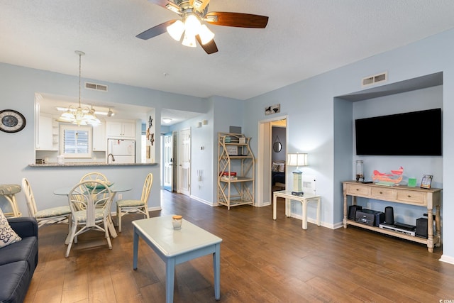 living room with ceiling fan, dark wood finished floors, baseboards, and a chandelier