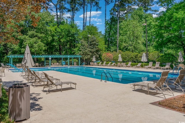 community pool with a patio area, a pergola, and view of scattered trees