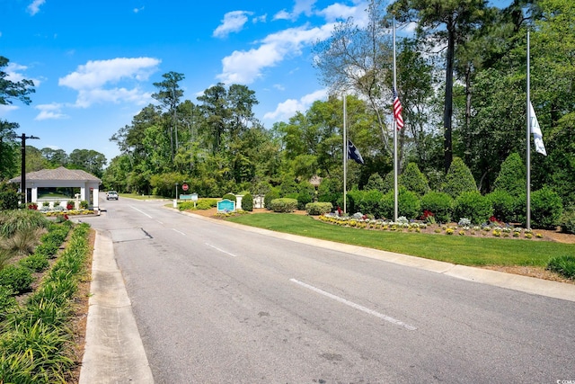 view of asphalt street with traffic signs, curbs, and view of scattered trees