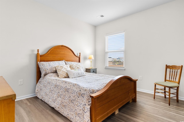 bedroom with baseboards, visible vents, and wood finished floors