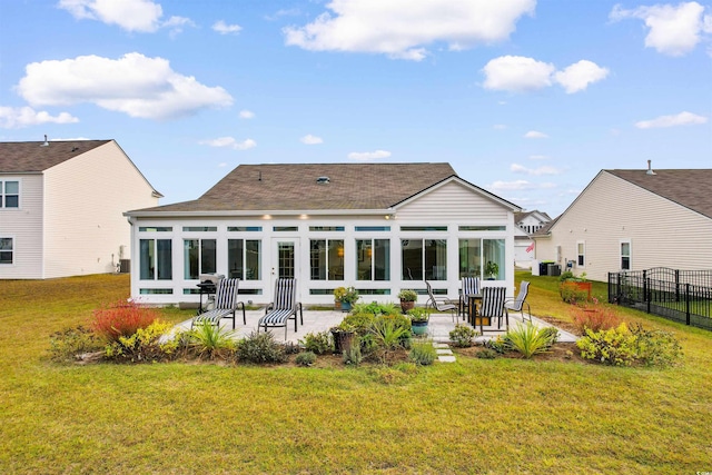 rear view of property featuring a sunroom, fence, a patio, roof with shingles, and a lawn