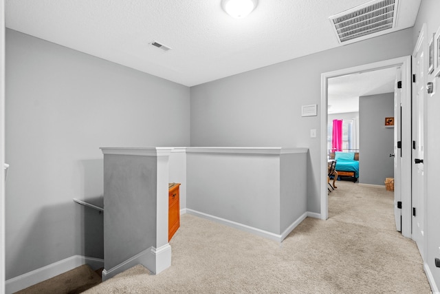 hall with an upstairs landing, carpet, baseboards, and a textured ceiling