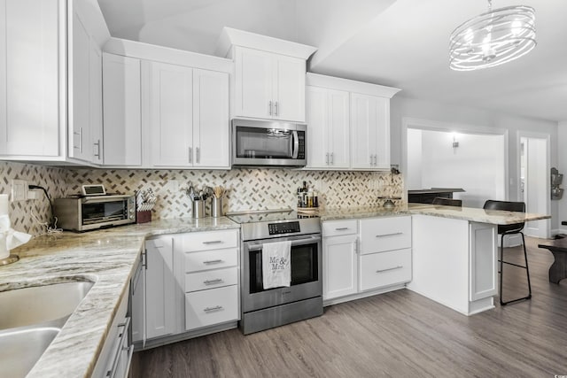 160 Shipmaster Ave, Pawleys Island, SC 29585 - kitchen with appliances with stainless steel finishes, a breakfast bar, light wood finished floors, white cabinets, and a peninsula