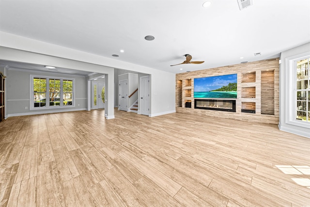 unfurnished living room with baseboards, a fireplace, stairs, a healthy amount of sunlight, and light wood finished floors
