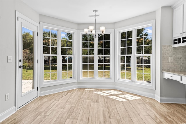 unfurnished dining area featuring light wood finished floors, baseboards, an inviting chandelier, and plenty of natural light