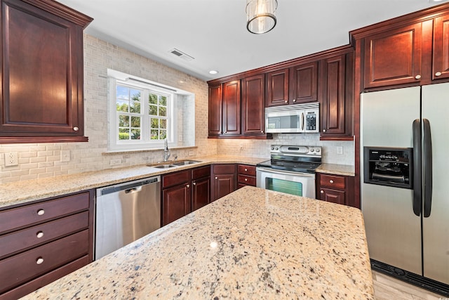 kitchen featuring visible vents, a sink, light stone countertops, decorative backsplash, and stainless steel appliances