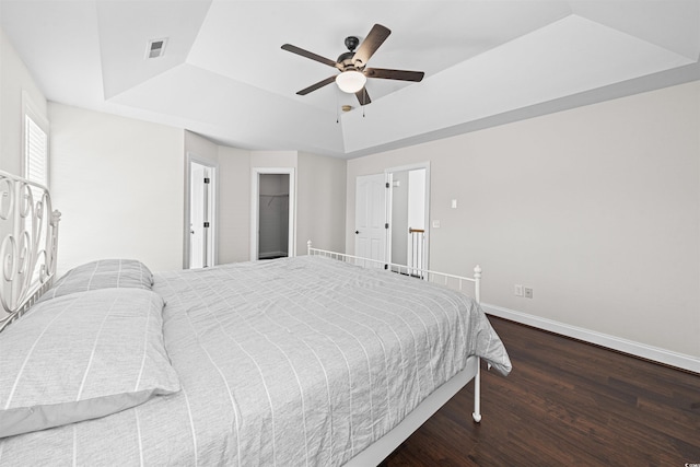 bedroom featuring ceiling fan, a tray ceiling, visible vents, wood finished floors, and baseboards