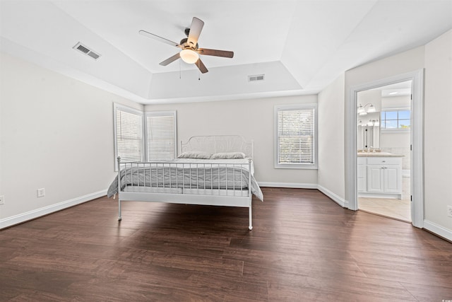 bedroom with a tray ceiling, wood finished floors, baseboards, and visible vents