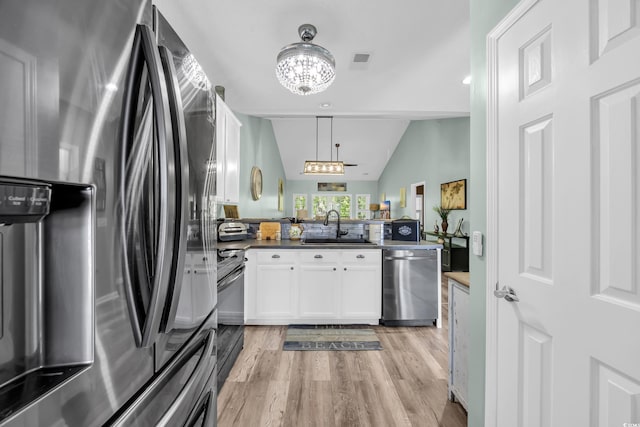 kitchen with a notable chandelier, vaulted ceiling, a peninsula, white cabinetry, and stainless steel appliances