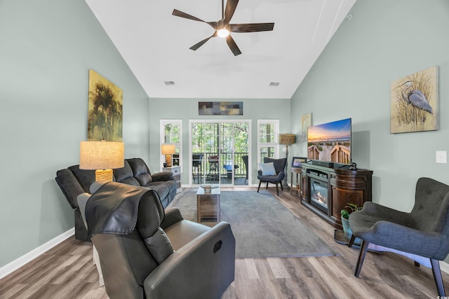 living area featuring a glass covered fireplace, high vaulted ceiling, wood finished floors, and ceiling fan