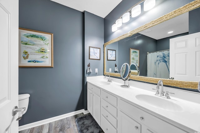 full bath with double vanity, baseboards, a sink, and wood finished floors