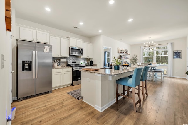 kitchen featuring stainless steel appliances, an island with sink, white cabinets, light wood finished floors, and a chandelier