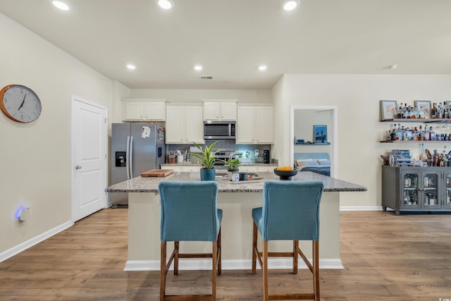 kitchen featuring stainless steel appliances, an island with sink, white cabinetry, a kitchen bar, and recessed lighting