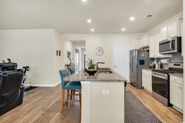 kitchen featuring stainless steel appliances, a sink, light wood-style floors, a kitchen bar, and an island with sink