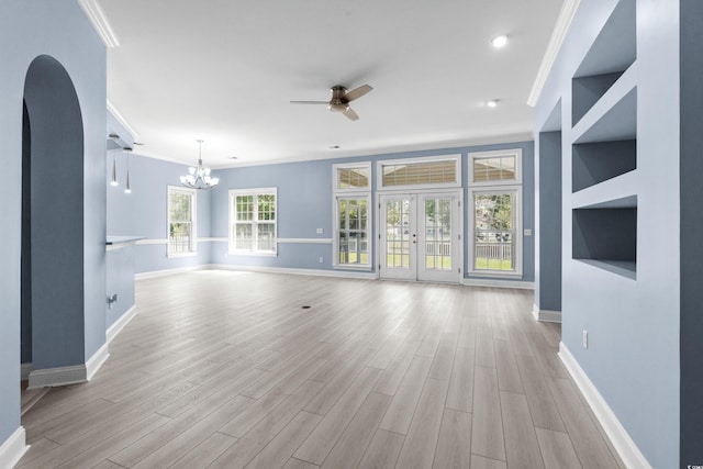 unfurnished living room featuring arched walkways, light wood-type flooring, baseboards, ceiling fan with notable chandelier, and crown molding