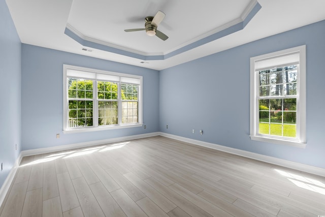 empty room featuring a raised ceiling, light wood-style flooring, a healthy amount of sunlight, and visible vents