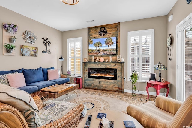 living room with a glass covered fireplace, wood finished floors, visible vents, and baseboards