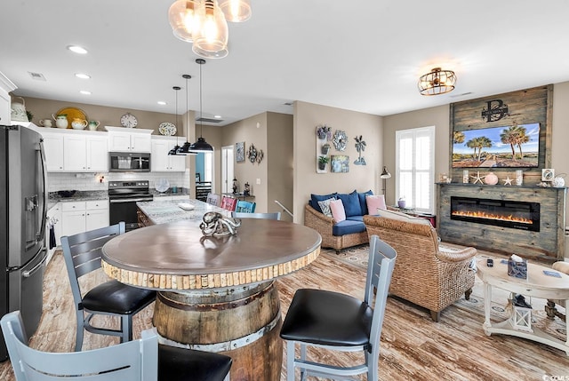 dining space with visible vents, light wood-style flooring, a glass covered fireplace, and recessed lighting