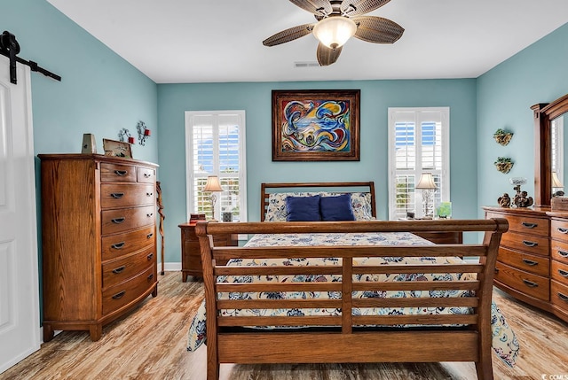 bedroom with a barn door, light wood-type flooring, visible vents, and multiple windows