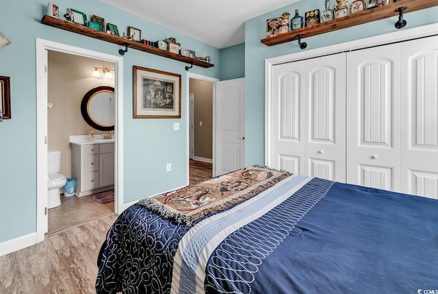 bedroom with connected bathroom, baseboards, wood finished floors, and a closet