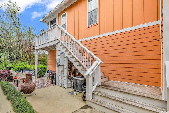 view of exterior entry featuring cooling unit, a patio area, and board and batten siding