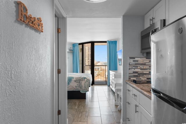 9550 Shore Dr Unit 1026, Myrtle Beach, SC 29572 - kitchen with appliances with stainless steel finishes, a textured wall, light tile patterned floors, white cabinetry, and tasteful backsplash