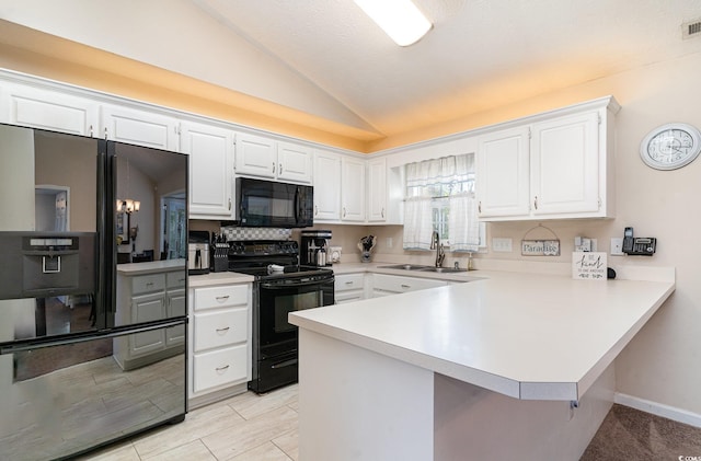 kitchen featuring a peninsula, light countertops, a sink, black appliances, and vaulted ceiling