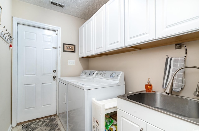 washroom featuring cabinet space, washer and dryer, a sink, a textured ceiling, and visible vents