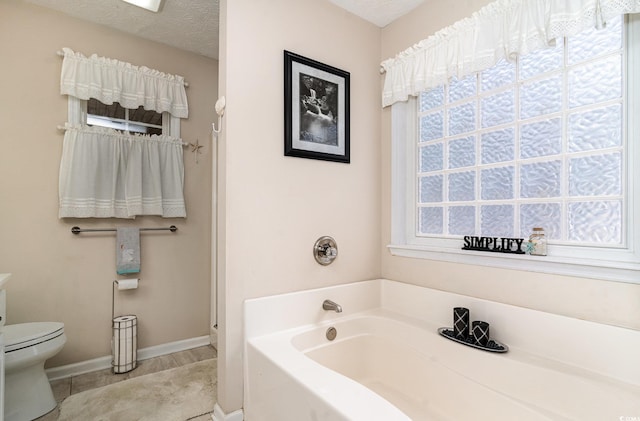 bathroom with baseboards, tile patterned flooring, toilet, and a bath