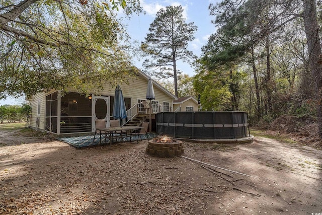 back of house with a wooden deck, a sunroom, a pool, a patio, and a fire pit