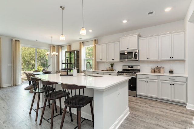 kitchen featuring an island with sink, a chandelier, a sink, light wood-style flooring, and stainless steel appliances