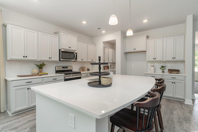 kitchen featuring decorative backsplash, a kitchen island with sink, white cabinetry, light wood finished floors, and stainless steel appliances