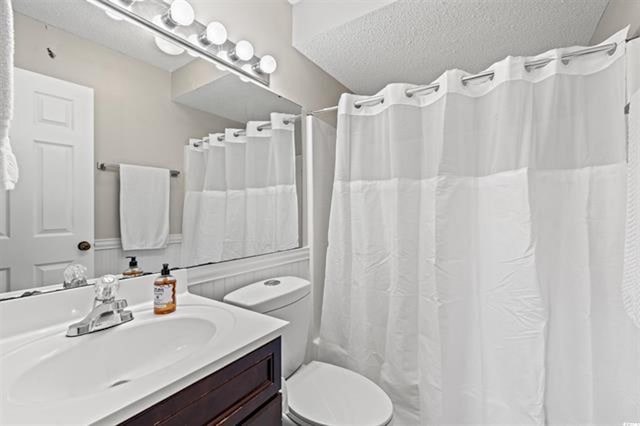 full bath with vanity, a textured ceiling, curtained shower, and toilet