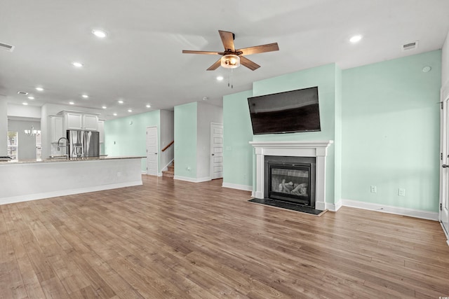 852 Harrison Mill St, Myrtle Beach, SC 29579 - unfurnished living room featuring a ceiling fan, light wood-style floors, recessed lighting, a glass covered fireplace, and stairway
