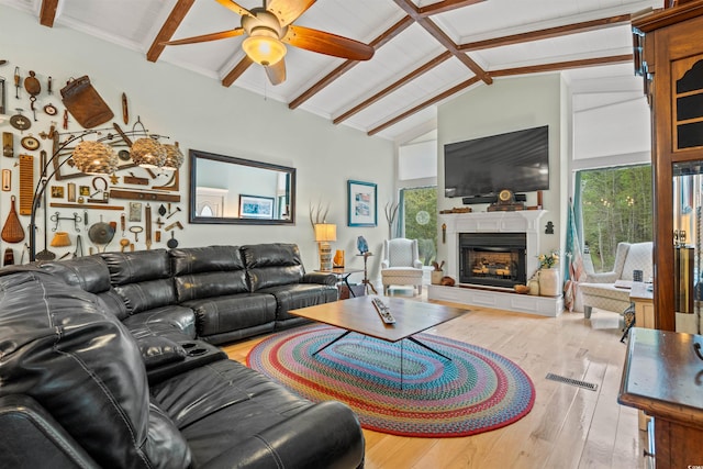 living area featuring a fireplace with raised hearth, a ceiling fan, vaulted ceiling with beams, visible vents, and hardwood / wood-style flooring