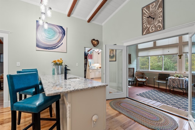 kitchen featuring wood finished floors, beamed ceiling, high vaulted ceiling, light stone counters, and a sink