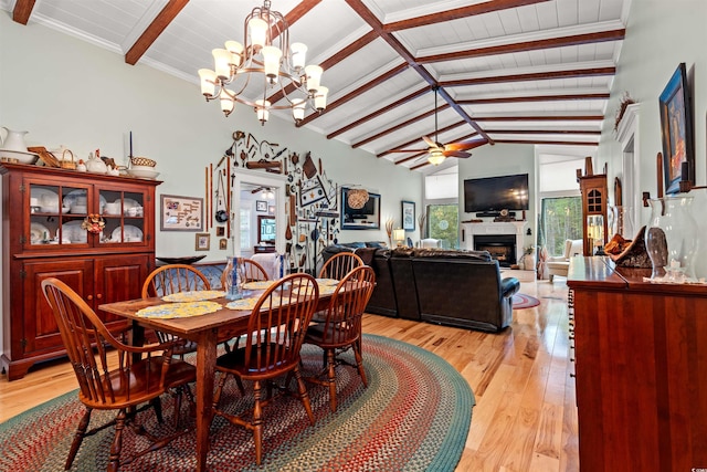 dining room featuring vaulted ceiling with beams, a fireplace, ceiling fan with notable chandelier, and light wood finished floors