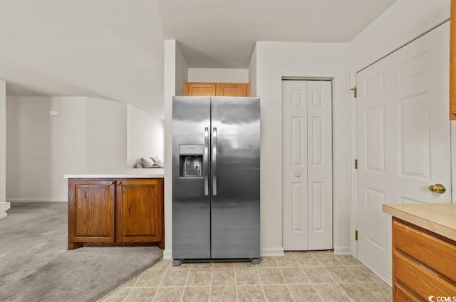 kitchen featuring light countertops, stainless steel refrigerator with ice dispenser, baseboards, a peninsula, and brown cabinets