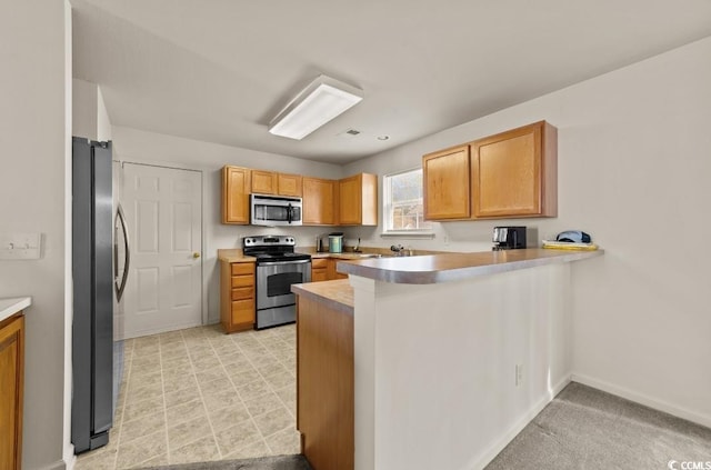 kitchen with baseboards, light countertops, a peninsula, and stainless steel appliances