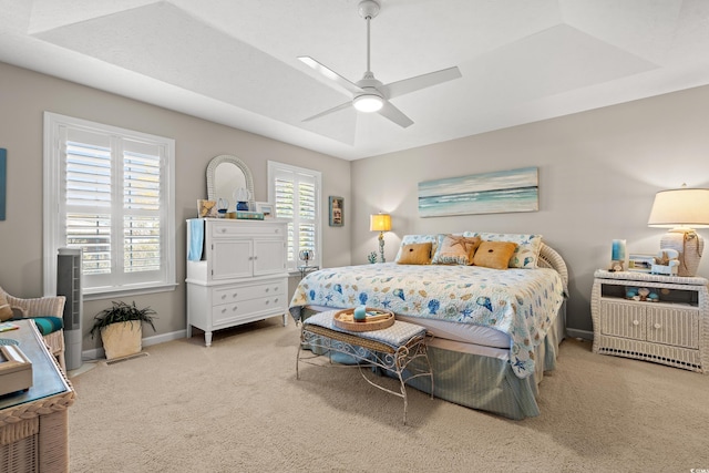 carpeted bedroom with a tray ceiling, baseboards, and a ceiling fan