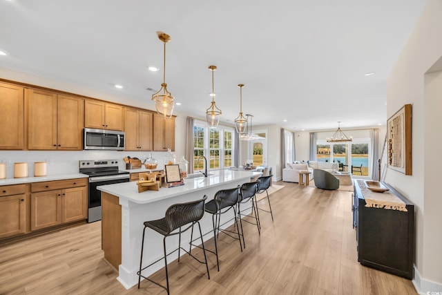 kitchen featuring stainless steel appliances, brown cabinets, light countertops, a breakfast bar, and a kitchen island with sink