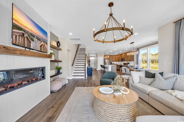 living room featuring a chandelier, dark wood-style flooring, stairway, a glass covered fireplace, and recessed lighting