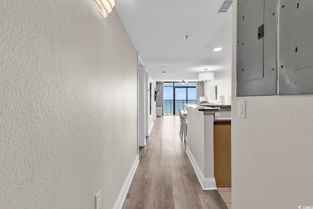 hallway with visible vents, light wood finished floors, baseboards, floor to ceiling windows, and a textured wall