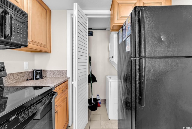 kitchen with light stone countertops, washer / clothes dryer, black appliances, and light tile patterned floors