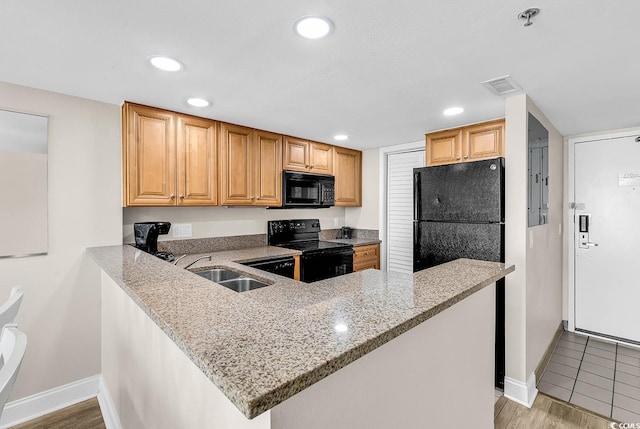 kitchen with light stone counters, a sink, a peninsula, visible vents, and black appliances